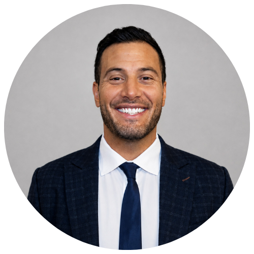Atmos Healthcare Man in a dark suit and tie smiling at the camera, standing against a plain light gray background.
